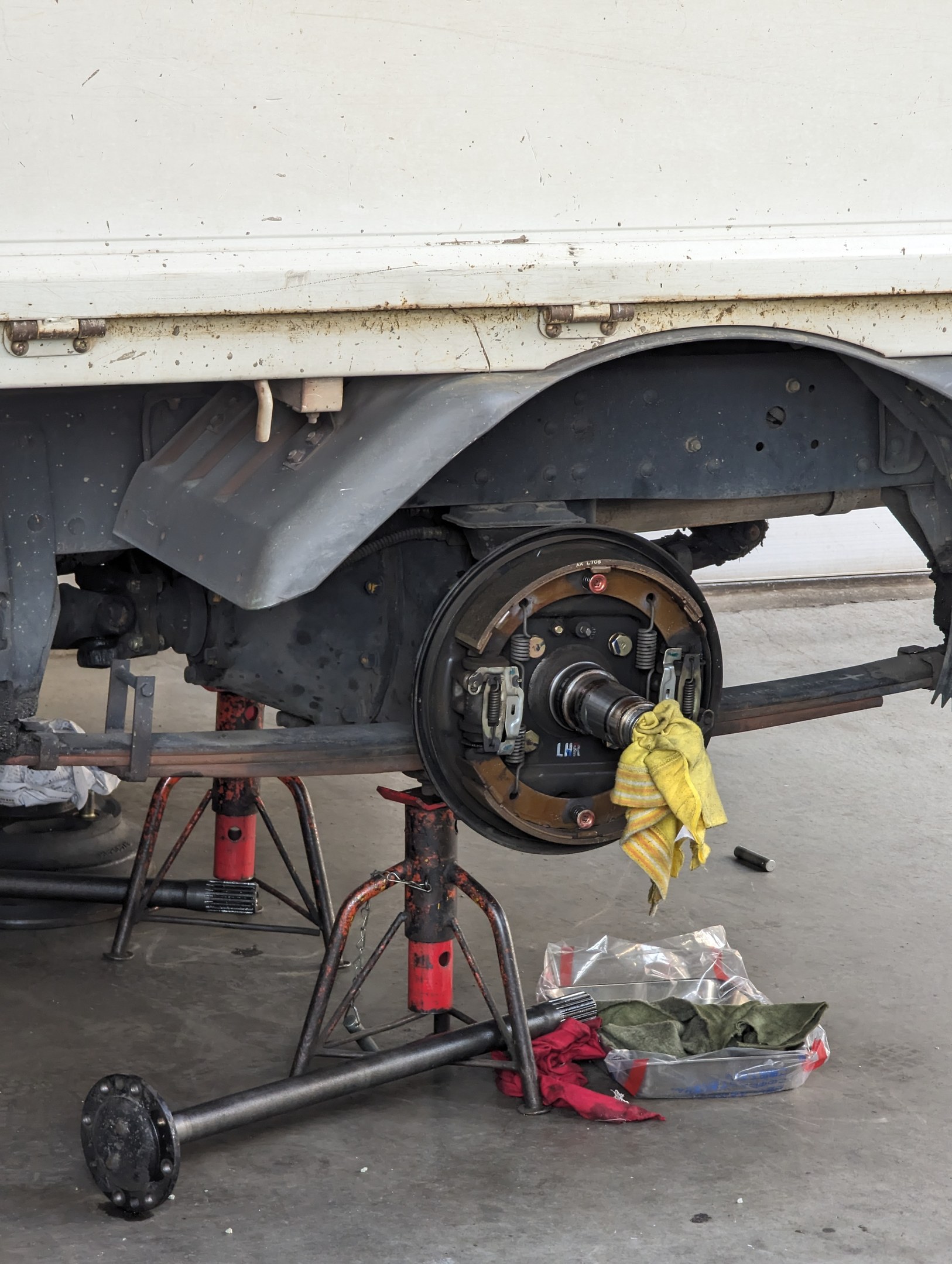 Ein gelbes Tuch liegt über einem in einer Garage geparkten Lkw, umgeben von Werkzeugen und Gegenständen auf dem Boden davor.