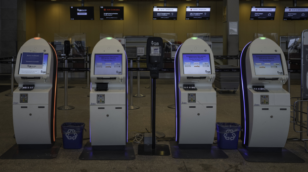 Eine Reihe von Geldautomaten auf einem gefliesten Boden, mit Mülltonnen, Pfosten, Tafeln mit Text, Lampen und anderen Gegenständen im Hintergrund.