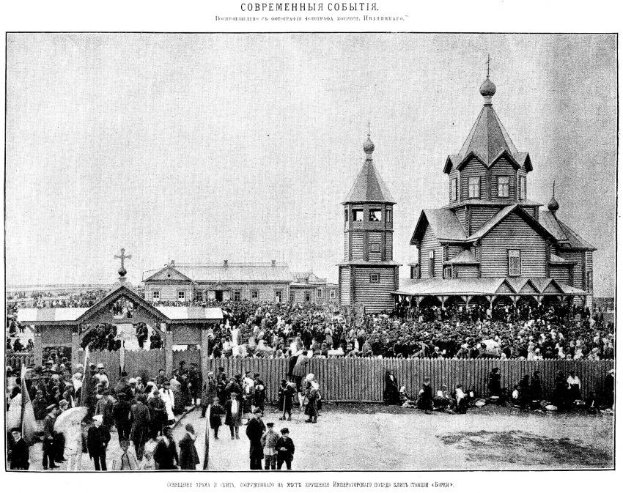 Schwarzes und weißes Foto einer Menschenmenge vor der Kirche der Versöhnung am Nerl mit einem hölzernen Zaun im Vordergrund und Gebäuden im Hintergrund.