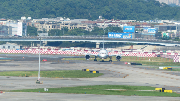 Flugzeug startet von einer Flughafenrollbahn mit umgebenen Infrastruktur, Wasser, Gebäuden, Bäumen und einem klaren blauen Himmel.