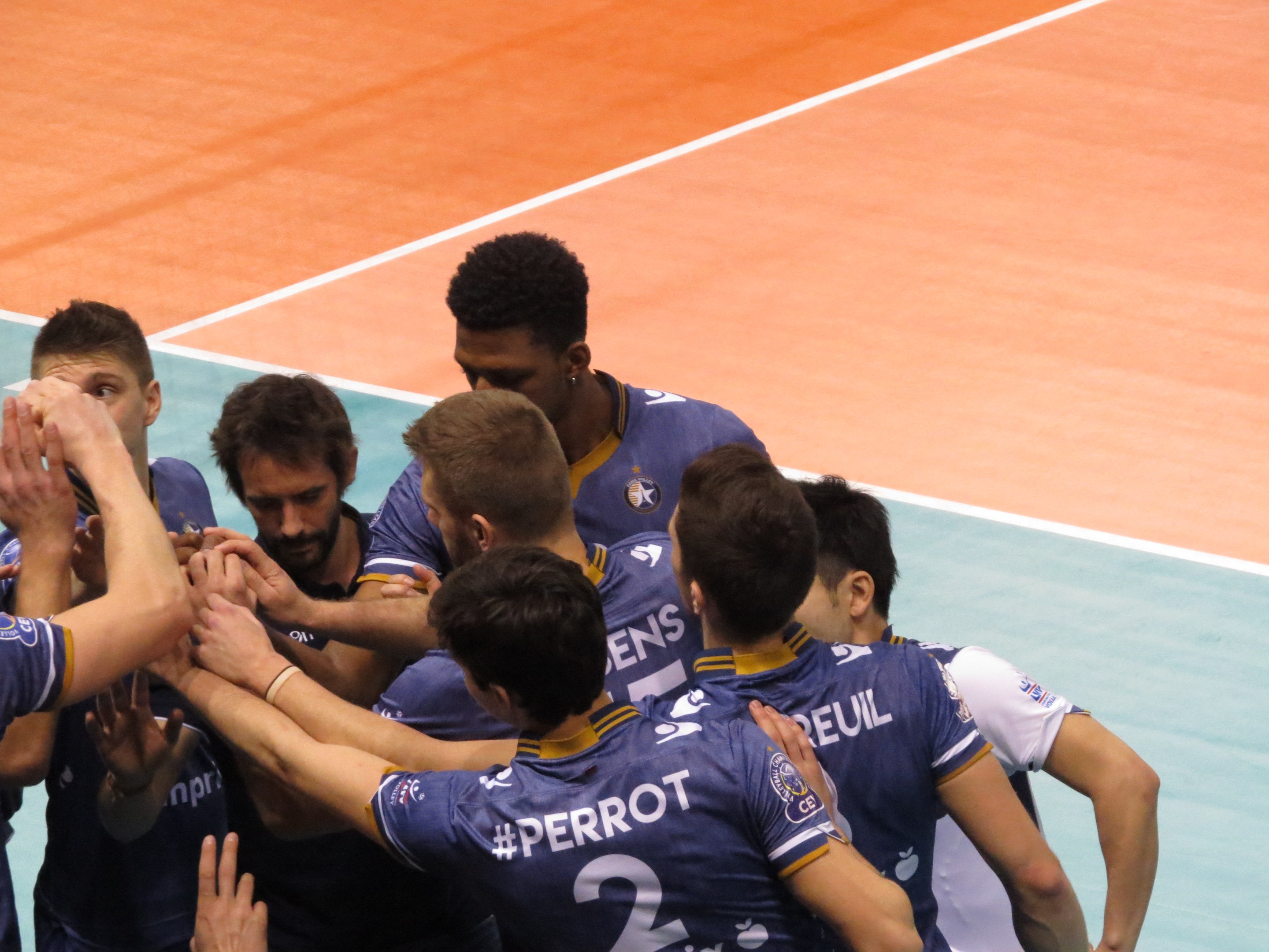 Gruppe von Männern in blauen "Ligue 1"-T-Shirts, die auf einem Volleyballfeld feiern.