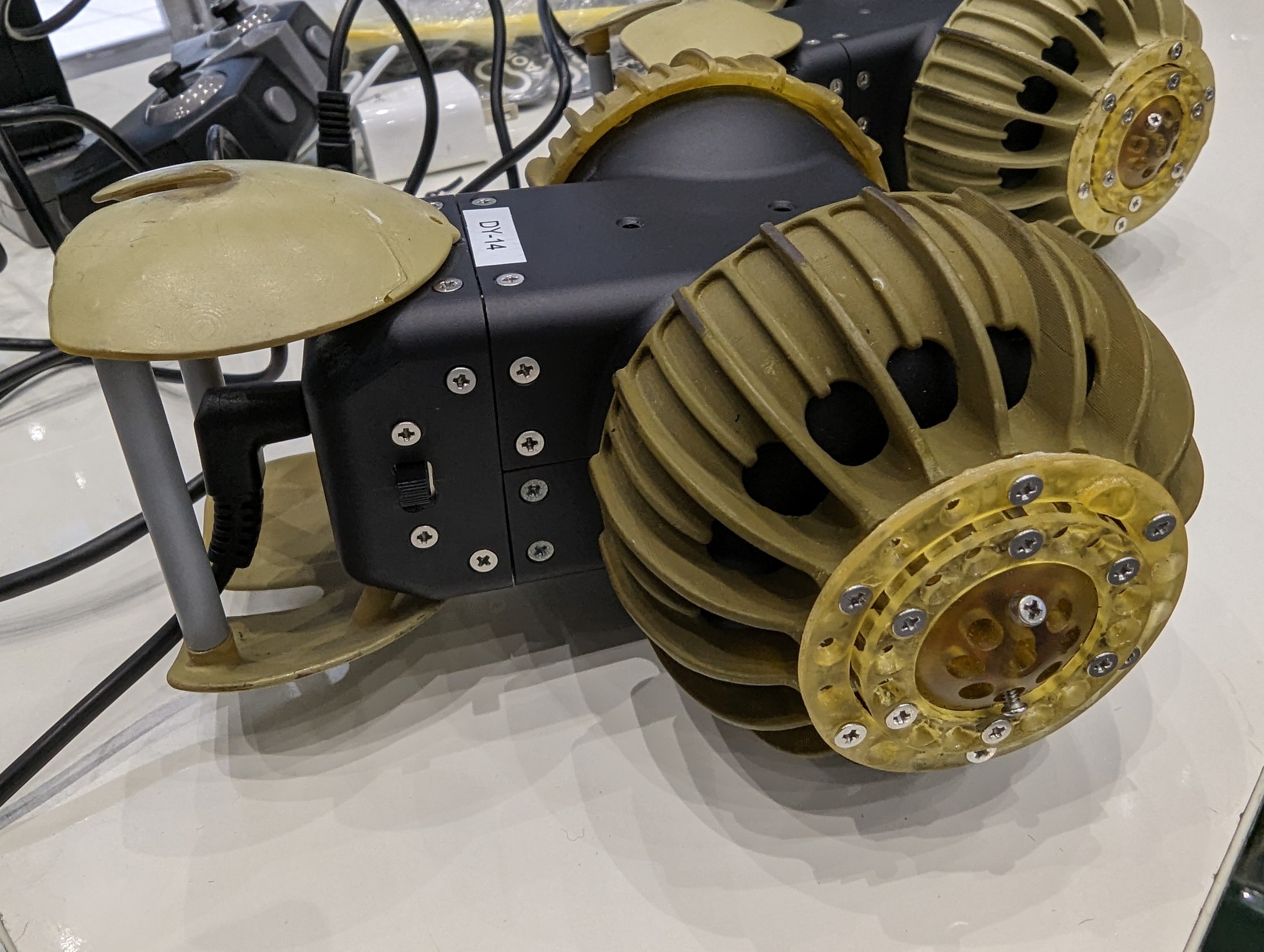 Nahaufnahme eines schlanken, metallischen 3D-gedruckten Roboters mit detaillierten Elementen auf einem Tisch umgeben von Drähten.