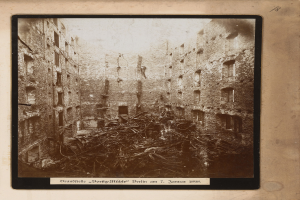 Ein Schwarz-Weiß-Foto eines stark beschädigten städtischen Gebäudes, gerahmt und umgeben von verstreuter Trümmer, mit schwach sichtbarem Text unten.