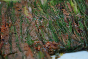 Nahaufnahme eines Steaks mit goldbrauner Kruste und saftigem Inneren neben zarten Spargelstangen auf einem weißen Teller, garniert mit Kräutern und Gewürzen.