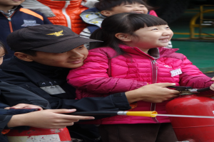 Gruppe von Kindern um ein rotes Feuerhydrant in einer Schulumgebung, ein Kind hält einen Schlauch.