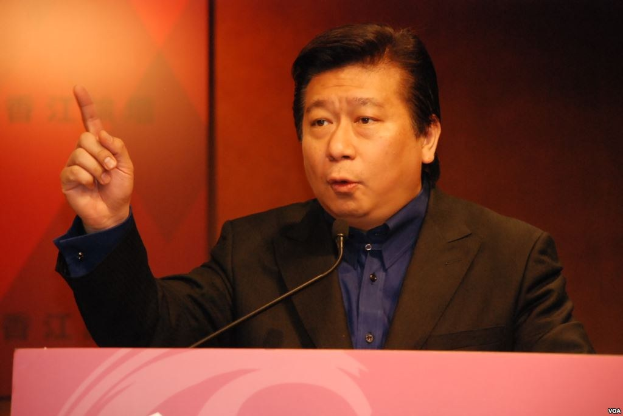 Ein Mann im Anzug und Krawatte, der eine Rede an einem Rednerpult mit einem Mikrofon hält und ernst aussieht.