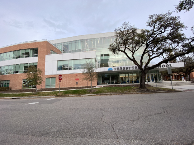 Großes, zweistöckiges Gebäude mit zahlreichen rechteckigen Fenstern, umgeben von Bäumen, Gras, Schildern, Strommasten und einer asphaltierten Straße, mit bewölktem Himmel im Hintergrund; als Presbyte Middle School beschriftet, geplant zur Eröffnung im Jahr 2020.
