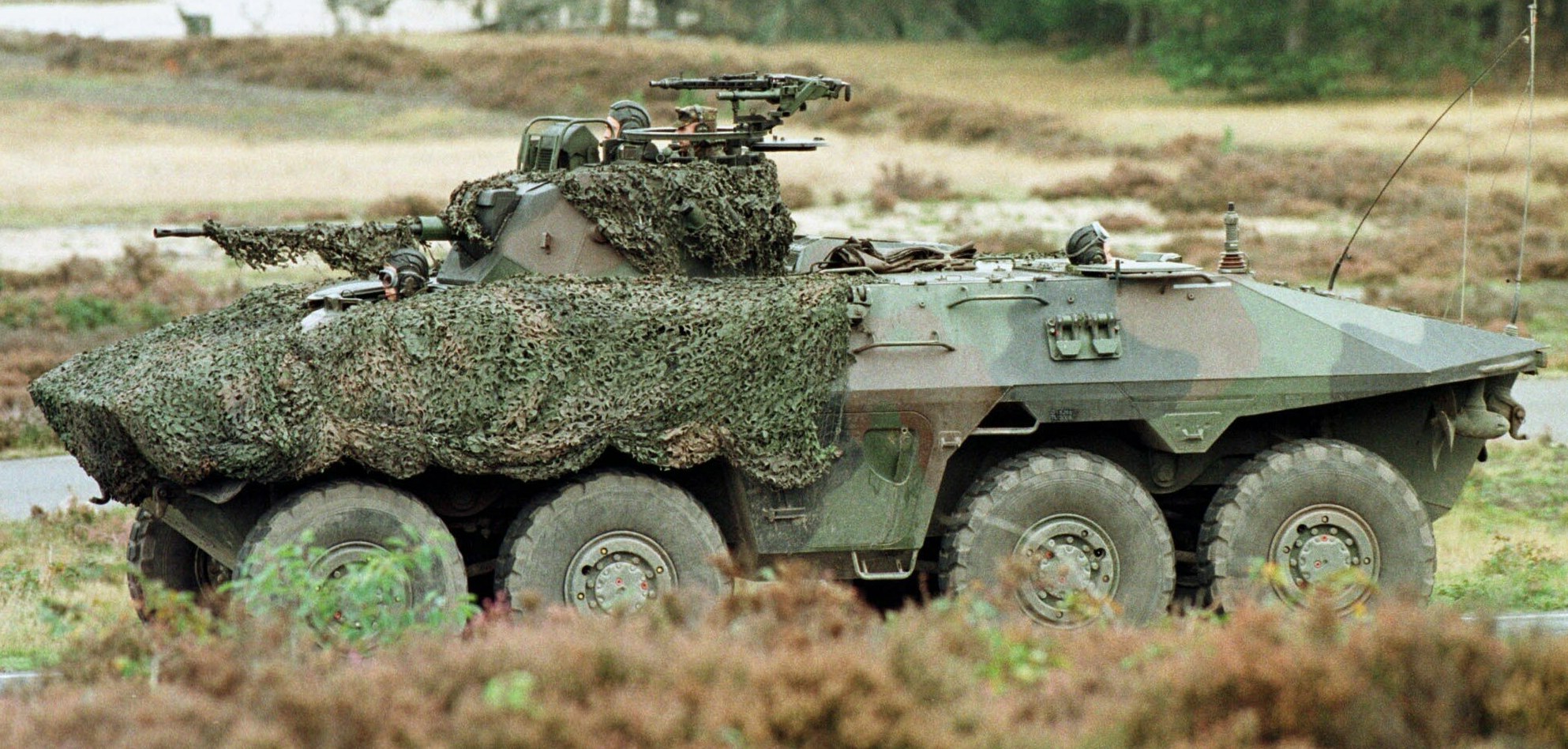 Militärpersonen-Transportfahrzeug mit montierter großer Kanone, das auf einer Straße neben einem Wald fährt.